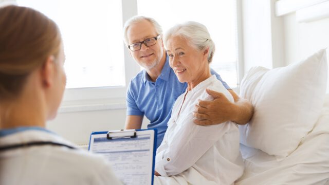 senior woman and doctor with clipboard at hospital